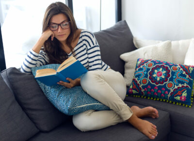 A woman reading a book while sitting on the couch.