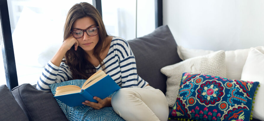 A woman reading a book while sitting on the couch.