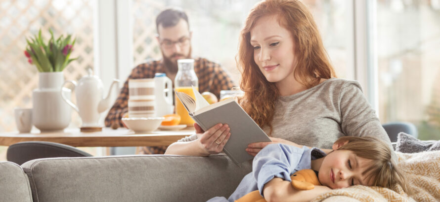 A woman reading a book while a child sleeps on her lap.