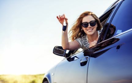 A girl leaning out of a car window holding the keys to a car.