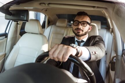 A man smiling while steering a car with one hand.