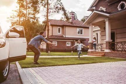 A child runs towards a smiling man in front of a car.