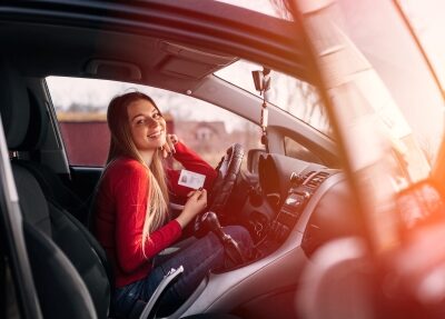 A woman inside a car smiles with through the open passenger door.