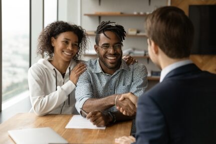 A couple shakes hands with a man after signing buying papers.