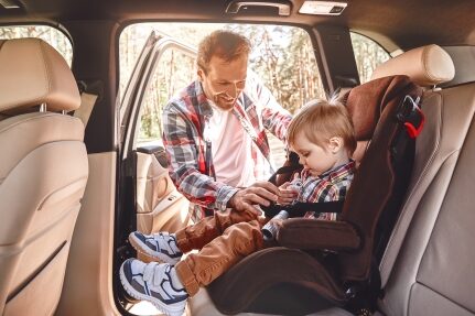 A man buckles his child into a car seat.