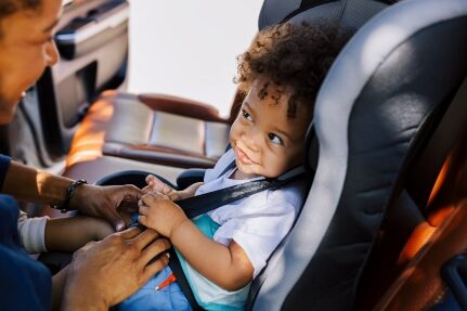 A woman buckles her child into a carseat.