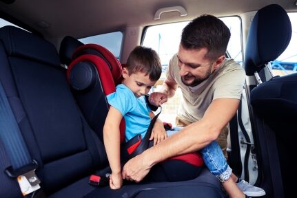 A man buckles his child in for a road trip.