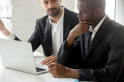 Two professional men look at a computer.