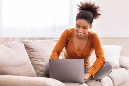 A woman looks at her computer on the couch.