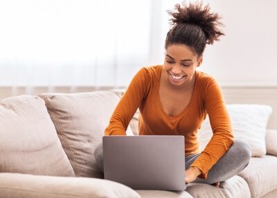 A woman looks at her computer on the couch.