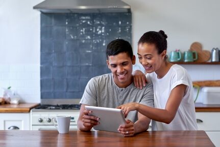 A couple reads from a tablet in the kitchen.