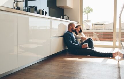 A couple sits on the kitchen floor of their home.