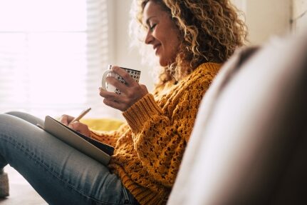 A woman writes while drinking coffee.