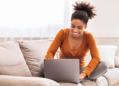 A woman works on a laptop on a couch.