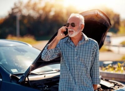 A man on the phone while the hood of the car is open.