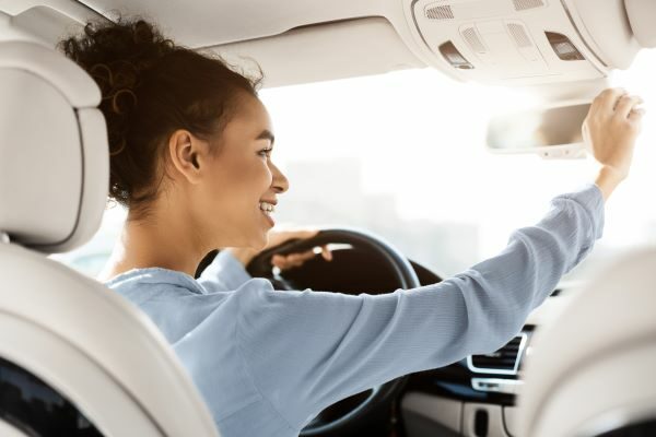 A woman happily adjusting her mirror in the car.