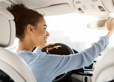 A woman happily adjusting her mirror in the car.