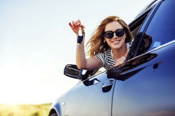 A woman holding out the key from the car window.