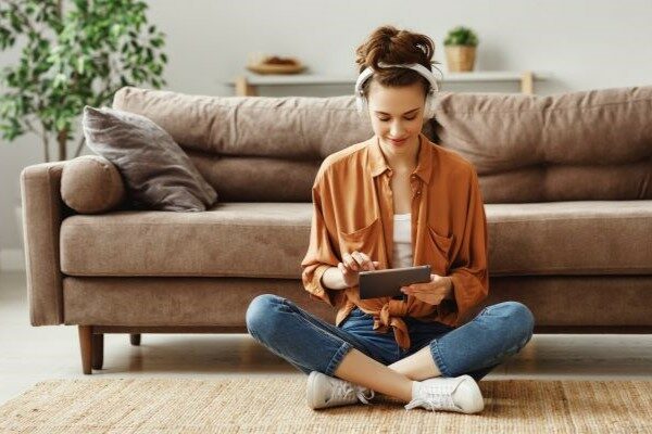 A woman using a tablet while sitting on a rug.