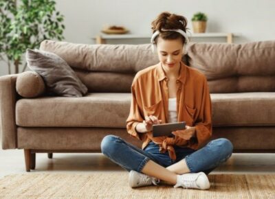 A woman using a tablet while sitting on a rug.