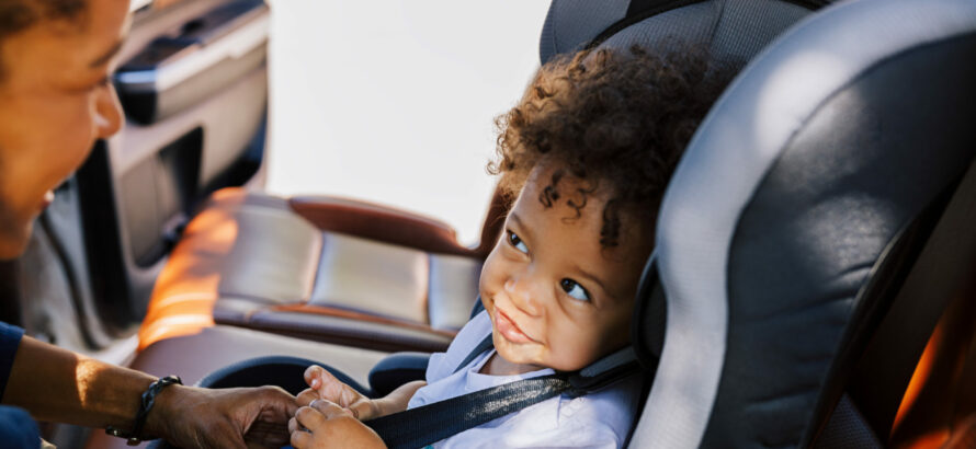 A child sitting in their car seat and smiling.