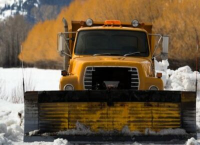 A dark yellow snow removal vehicle parked in the snow.