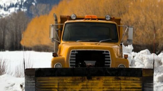 A dark yellow snow removal vehicle parked in the snow.