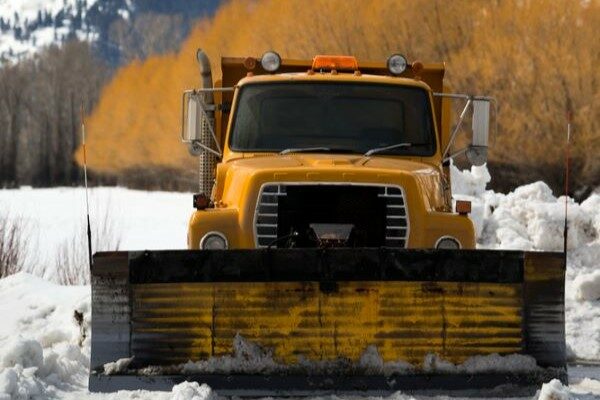 A dark yellow snow removal vehicle parked in the snow.