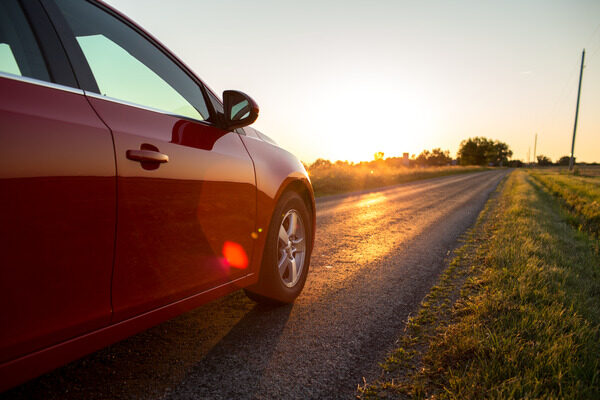 A red car drives down a country road at sunset.