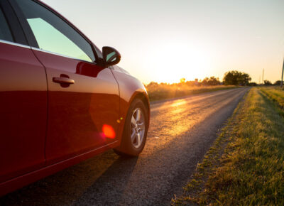 A red car drives down a country road at sunset.