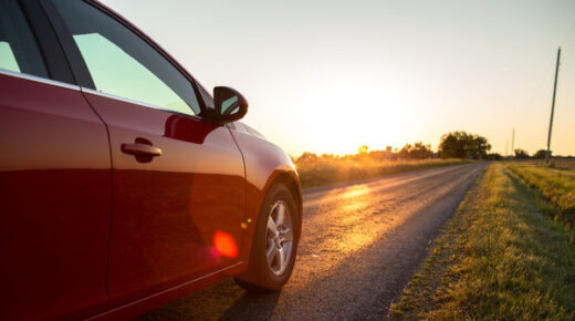 A red car drives down a country road at sunset.