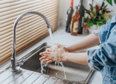 A woman washing her hands in the kitchen sink.