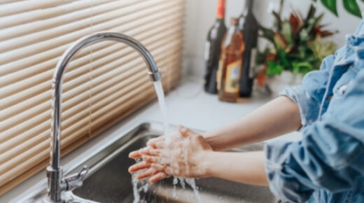 A woman washing her hands in the kitchen sink.