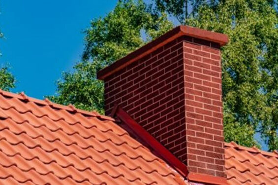 A red brick chimney sitting on top of a terra cotta tile roof.