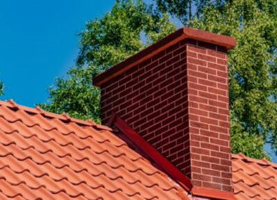 A red brick chimney sitting on top of a terra cotta tile roof.