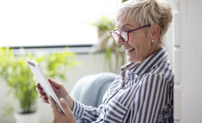 A woman with glasses smiles at her tablet.