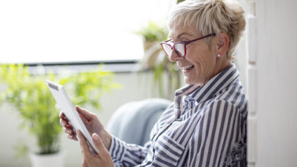 A woman with glasses smiles at her tablet.
