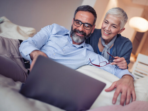 A couple smiles at their laptop.