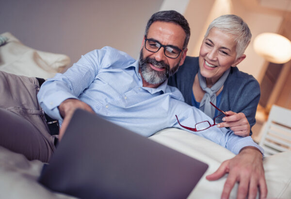 A couple smiles at their laptop.