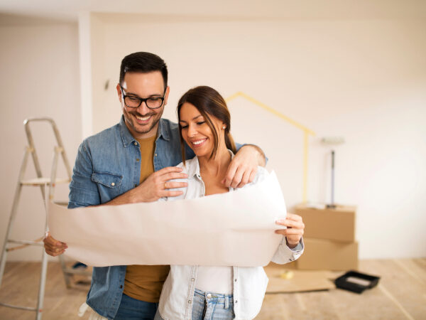 A young couple stands in their home, looking at blueprints.