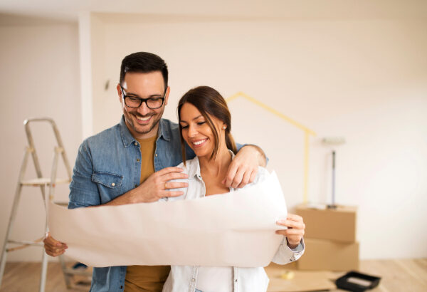 A young couple stands in their home, looking at blueprints.