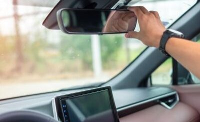 A hand adjusting a car’s rearview mirror from the driver’s seat.