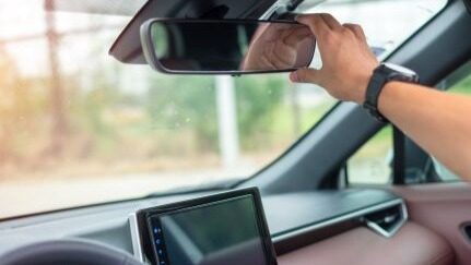 A hand adjusting a car’s rearview mirror from the driver’s seat.