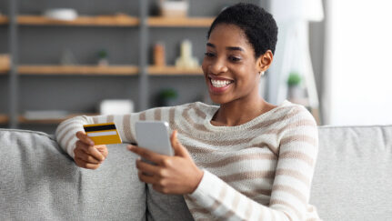 A woman happily holds a credit card in one hand and her mobile device in her other hand.