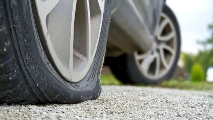 A car with a flat front tire resting on a gravel surface.