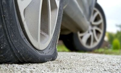 A car with a flat front tire resting on a gravel surface.